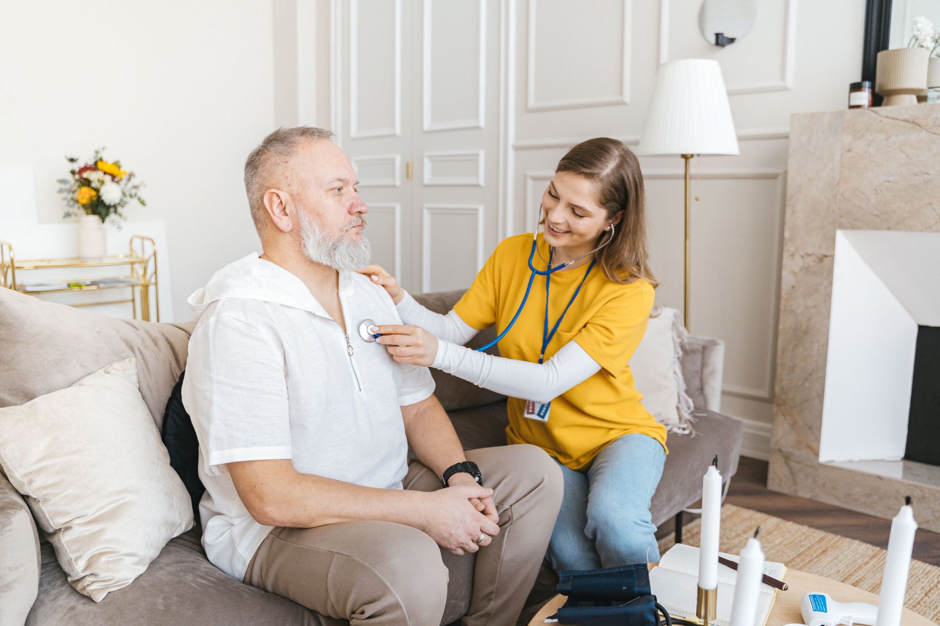 A nurse listening to an older man’s heart with a stethoscope in his living room