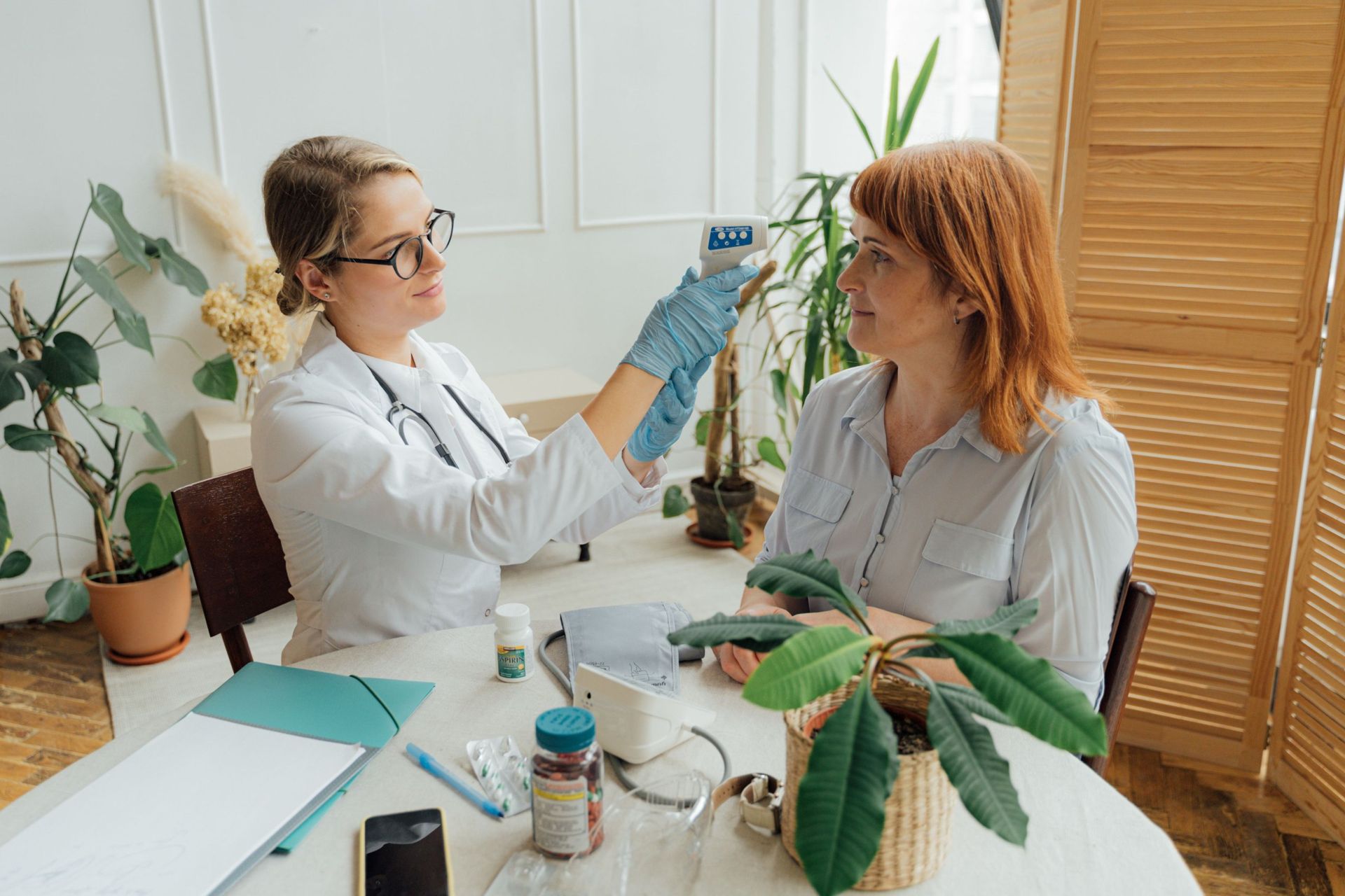 A physician checking a patient’s temperature at her dining table at home